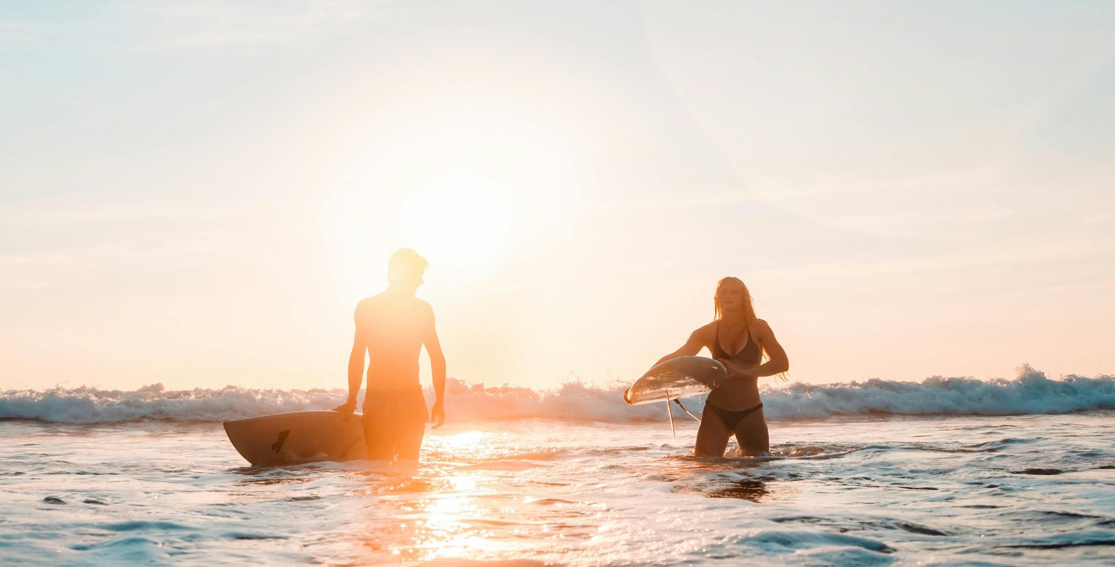 A man and woman surfing at sunset.