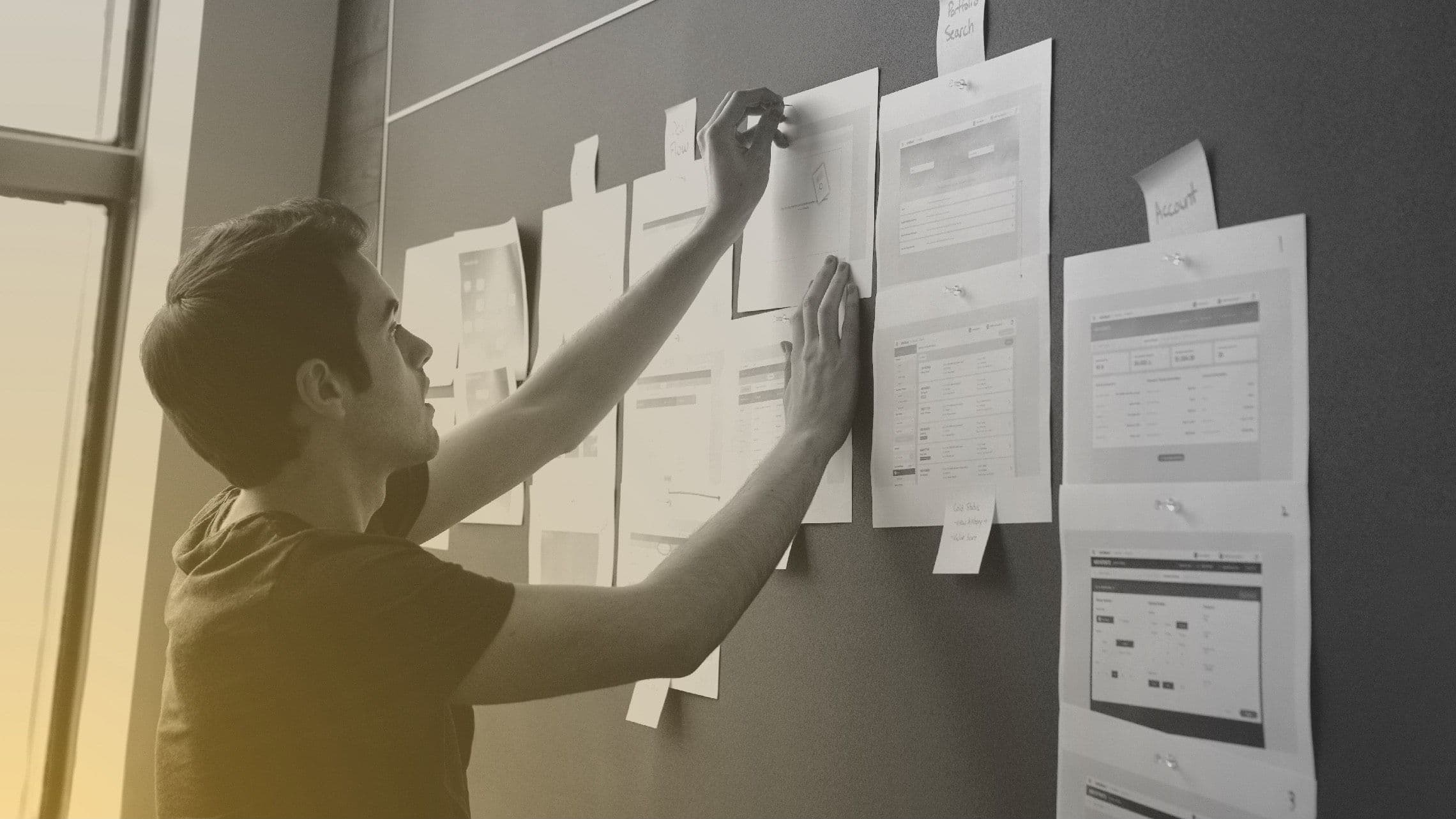 Photograph of a designer pinning paper to a corkboard.