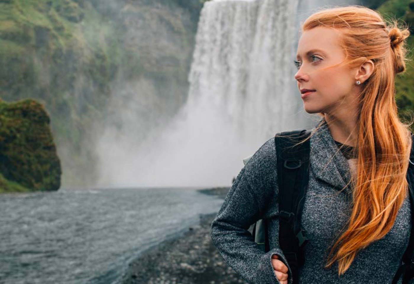 Photograph of a girl standing near a waterfall.