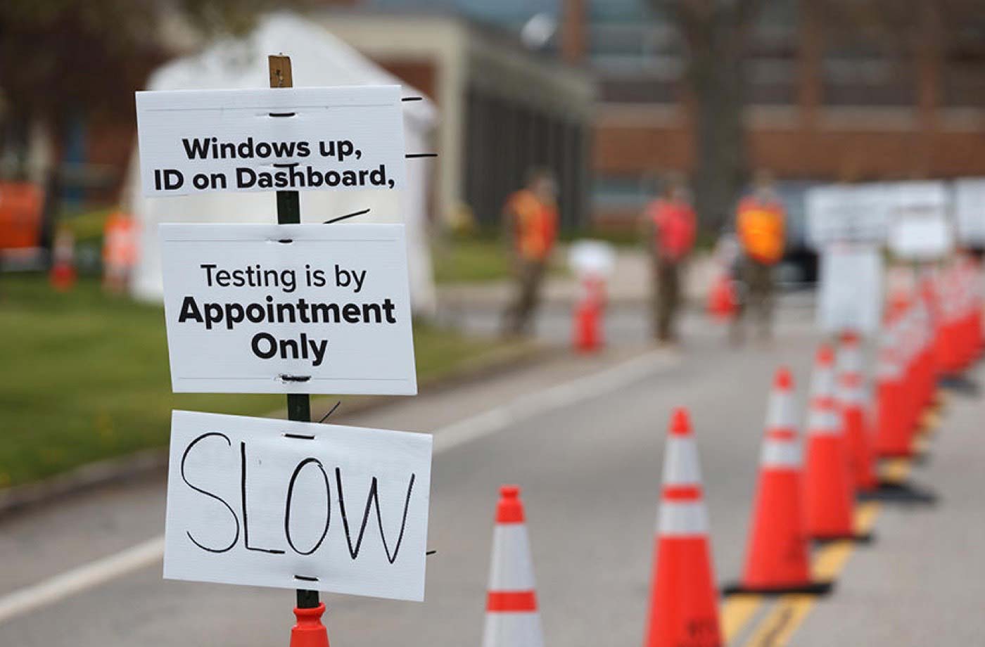 Photograph of signs for a testing site - "Windows up. ID on dashboard. Testing is by appointment only. Slow."